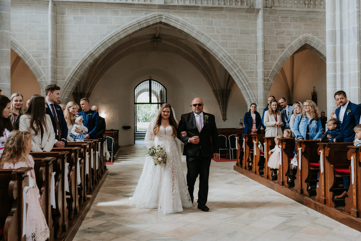 The bride walks down the aisle with her father.