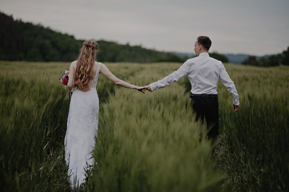 95_resort-chobot-wedding-photographer-monika-chano The bride and groom walk through a field during their photo shoot.
