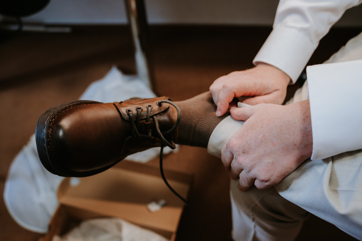 The groom puts on his shoes during wedding preparations.